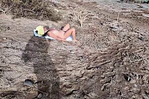 A daring spy follows a voluptuous naturist at the beach